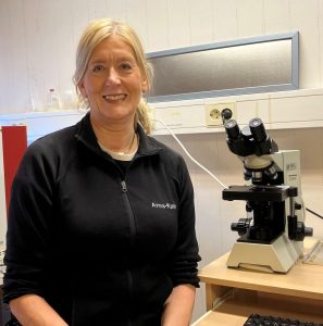 Kvinna i mörk tröja sitter bredvid mikroskop